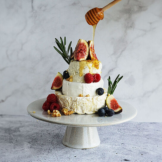 Herzhaft-süße Käsetorte ohne Boden mit Früchten und Nüssen Kunstvoll arrangierte Käsetorte ohne Boden, geschichtet mit Camembert, Saint André und BRESSO, garniert mit frischen Feigen, Himbeeren, Heidelbeeren und Rosmarinzweigen.