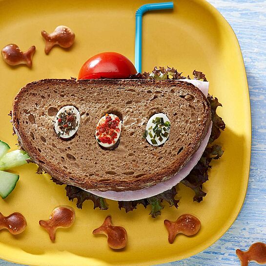Pfiffiges Pausenbrot als lustiges U-Boot serviert mit Tomate, Gurke und Fischbrezeln