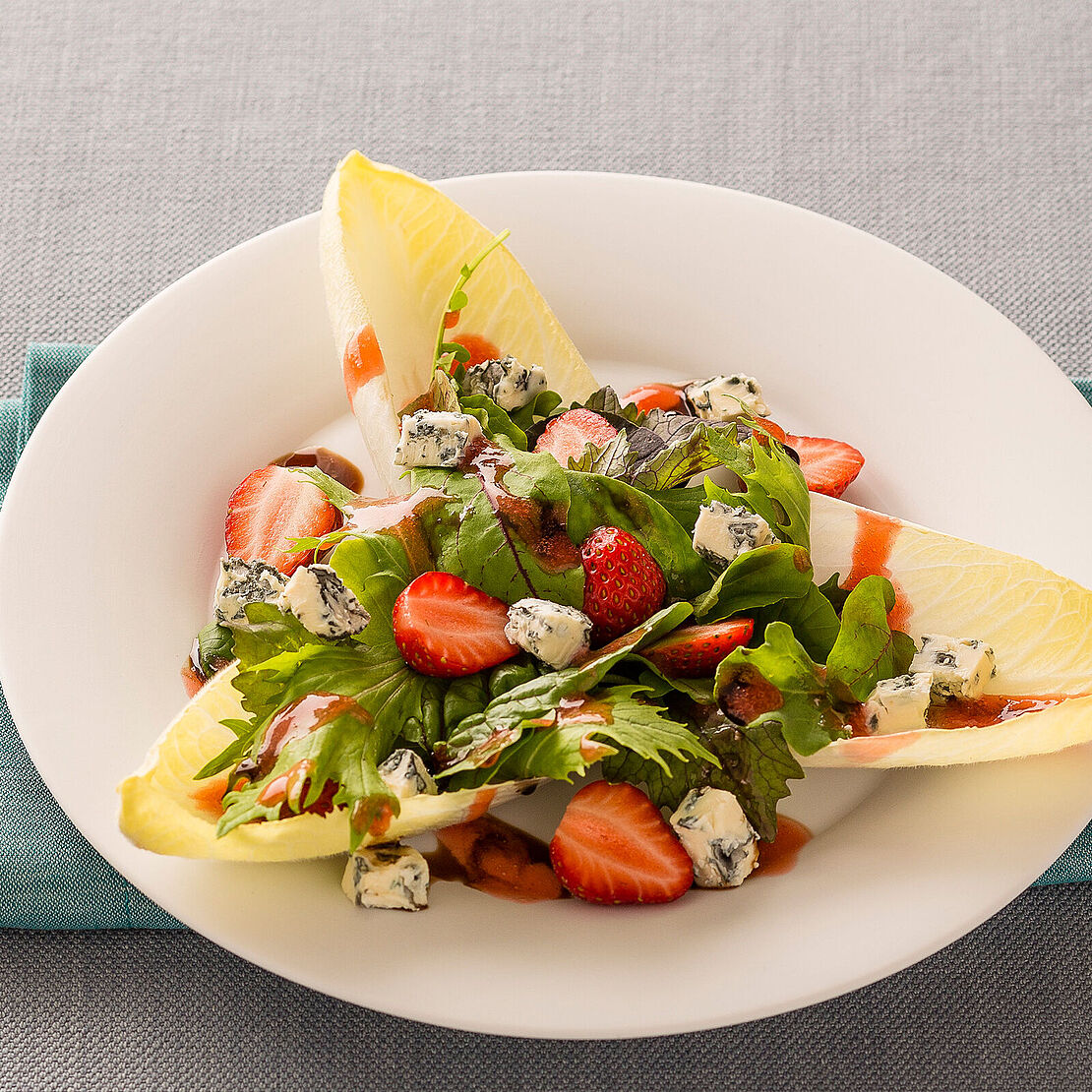 Leckerer Salat mit Erdbeeren, Chicoree, Feldsalat und Blauschimmelkäse auf einem weißen Teller serviert 