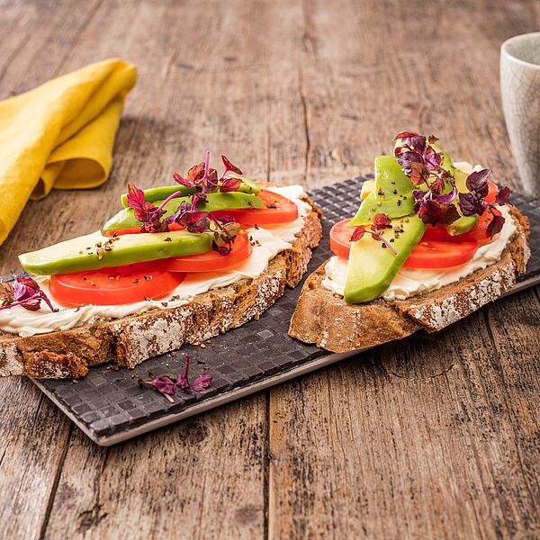 Frisches Bauernbrot mit Brunch Original Natur Käse, saftigen Tomaten und leckerer Avocado. Garniert mit Sprossen.