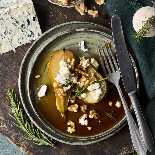 Elegant angerichtete pochierte Birnenhälften mit cremig würzigem Saint Agur, Honigsirup und gerösteten Walnüssen.
