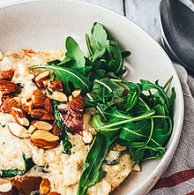 Das Ofenrisotto wird mit Reis, Gemüsebrühe, Salzmandeln, saftigen Kirschtomaten und frischem Rucola zubereitet,