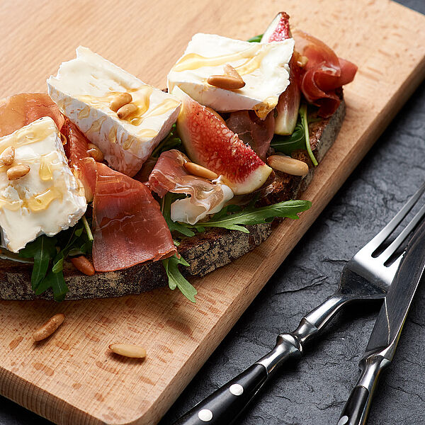 Deftige Brotzeit: Bauernbrot mit geräuchertem Schinken, Feigen, Pinienkernen, Käse und Honig. 