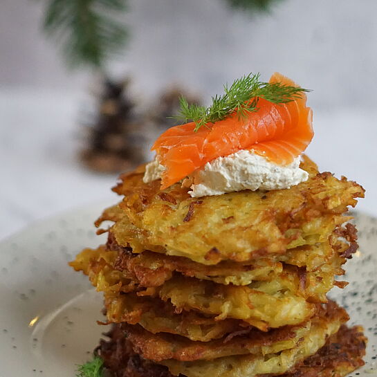 Frisch gebratene Kartoffelpuffer, garniert mit Räucherlachs und BRESSO Wildkräutern, serviert auf einem Teller.