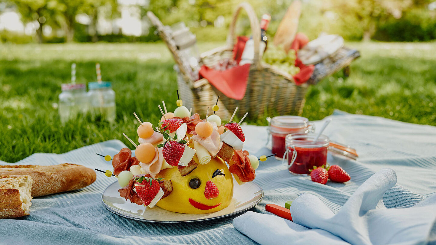 Käseigel Gérard hat auf seinen Spießen Géramont, Honigmelone und Putenbrust und sitzt auf einer Picknickdecke