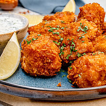 Ein Teller mit knusprig gebratenen Chicken Nuggets, gefüllt mit schmelzendem Käse, daneben ein frischer Dip.