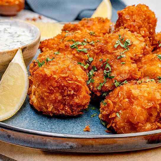 Ein Teller mit knusprig gebratenen Chicken Nuggets, gefüllt mit schmelzendem Käse, daneben ein frischer Dip.