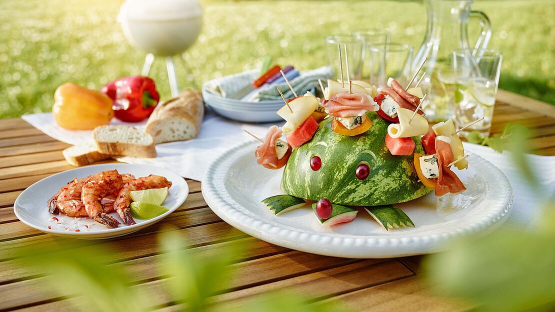 Käseigel Sunny mit Saint Agur, Fol Epi, Parmaschinken und Wassermelone bestückt sitzt auf einem Gartentisch