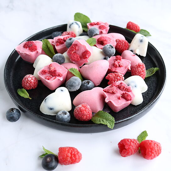 Kleine, gefrorene Joghurt-Beeren-Bites mit frischen Himbeeren und Heidelbeeren in Eiswürfelformen angerichtet
