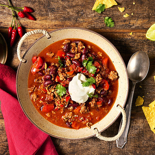 Rustikales Chili con Carne auf klassische Art in einer großen Schüssel mit Griffen. Getoppt mit Brunch Frischkäse