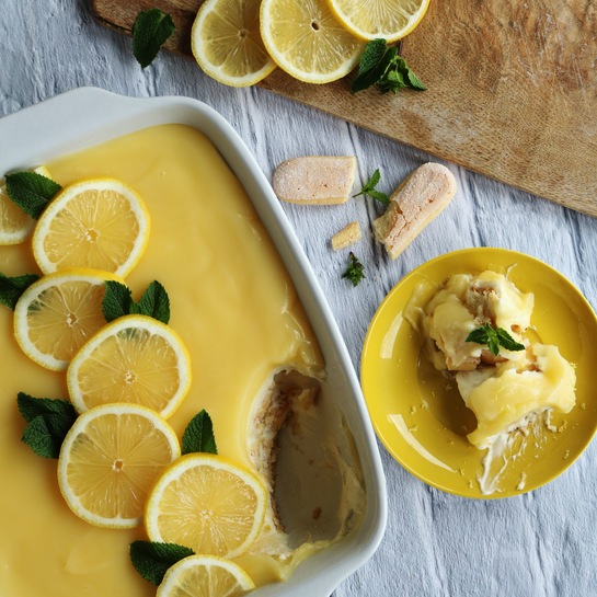 Ein frisch zubereitetes Zitronen-Tiramisu mit Limoncello in einer weißen Auflaufform, garniert mit Zitronenscheiben und Minzblättern.