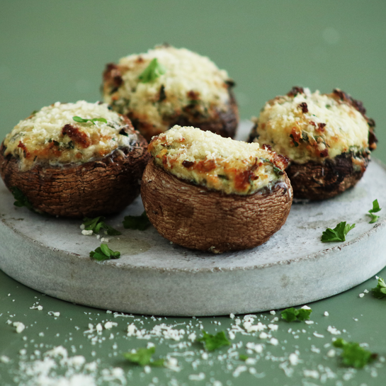 Rezept: Gefüllte Pilze aus dem Airfryer – mit Frischkäse knusprig überbacken Vier goldbraun überbackene, gefüllte Pilze mit cremiger Frischkäse-Kräuter-Füllung auf einem grauen Teller, bestreut mit Parmesan und Petersilie.