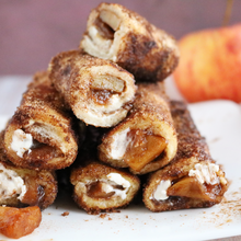 Apfel-Zimt-Toaströllchen mit Frischkäse Gestapelte Apfel-Zimt-Toaströllchen mit Frischkäsefüllung auf einem weißen Teller, gefüllt mit karamellisierten Apfelstücken und umhüllt von einer Zimt-Zucker-Kruste.