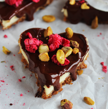 Cheesecake-Herzen mit Schokoladen-Topping und edler Garnitur Herzförmige Cheesecakes mit knusprigem Keksboden, cremiger Füllung und glänzendem Schokoladenüberzug, dekoriert mit Pistazien, Himbeeren und Kokoschips.